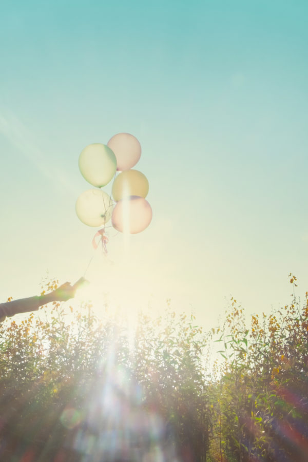 Girl running on the field of yellow flowerwith balloons at sunset. Happy woman on nature, concept about carefree airiness and relax, vintage effect.