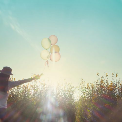 Girl running on the field of yellow flowerwith balloons at sunset. Happy woman on nature, concept about carefree airiness and relax, vintage effect.